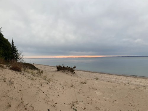 A serene beach scene with soft sand, gentle waves, and a cloudy sky reflecting a hint of sunset on the horizon.