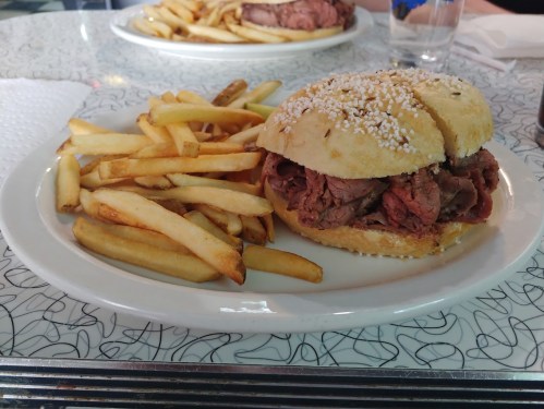 A plate with a sesame seed bun filled with roast beef, accompanied by a side of golden French fries.
