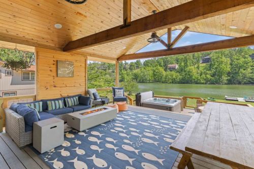 Cozy outdoor living space with a sofa, coffee table, and hot tub, overlooking a serene river and lush greenery.