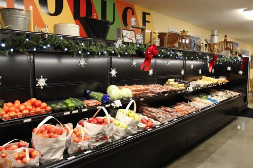 A grocery store display with fresh produce, including apples, cucumbers, and cabbage, decorated for the holidays.