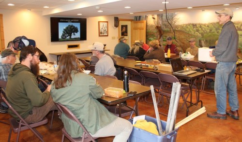 A group of people seated in a classroom setting, listening to a speaker with a presentation on a screen.