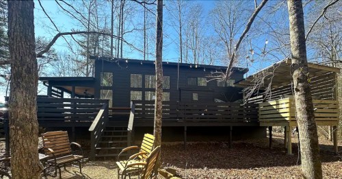 A modern black cabin surrounded by trees, featuring a deck and outdoor seating in a serene forest setting.