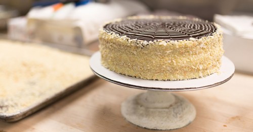 A beautifully decorated cake with a chocolate topping and almond flakes, displayed on a white cake stand.