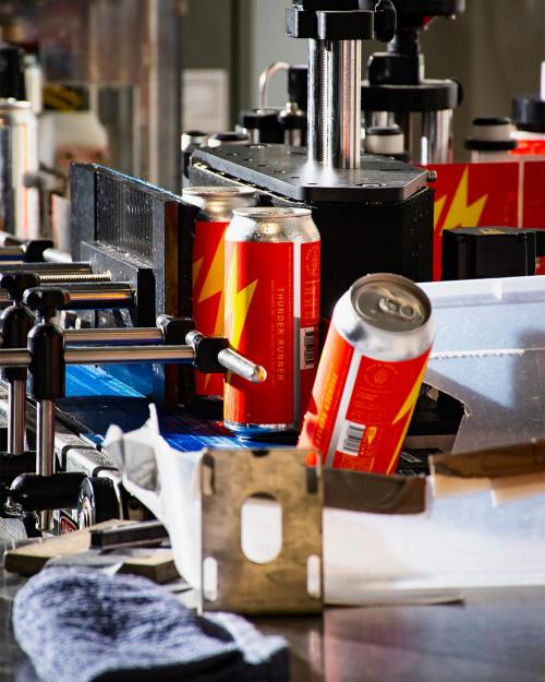 Cans of brightly colored beverage on a production line, with machinery and tools in the background.