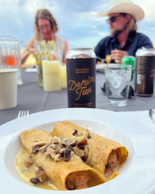 A plate of enchiladas with mushrooms in a creamy sauce, with people dining in the background at an outdoor setting.