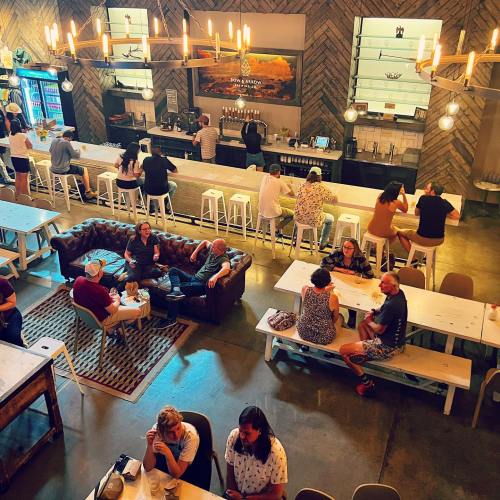 A lively bar scene with people socializing at tables and a long bar in a stylish, rustic setting.