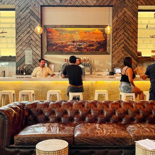 A cozy bar scene with a wooden counter, patrons sitting on stools, and a leather couch in the foreground.