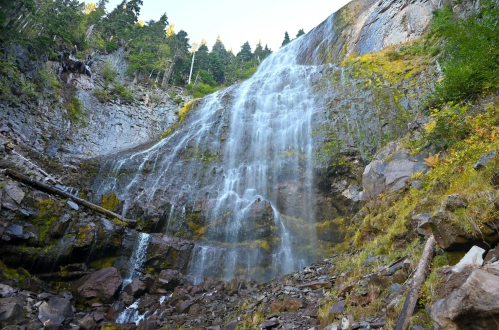 A cascading waterfall flows down rocky cliffs, surrounded by lush greenery and trees.