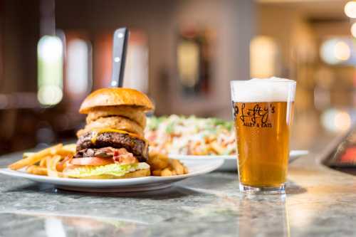 A gourmet burger with onion rings, fries, and a salad, alongside a frothy beer in a branded glass.