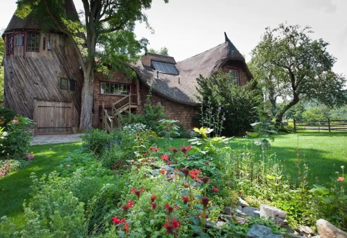 A charming, rustic house with a thatched roof surrounded by vibrant flowers and lush greenery.