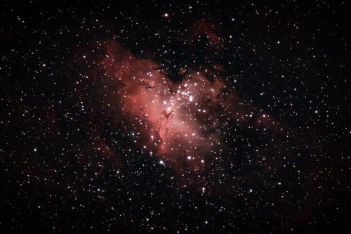 A vibrant nebula surrounded by stars, showcasing shades of red and pink against a dark cosmic background.