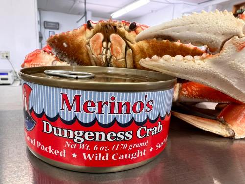 A can of Merino's Dungeness Crab next to a large Dungeness crab, showcasing the product and its fresh catch.