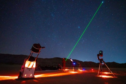 A stargazing scene with telescopes and a green laser pointing at the night sky filled with stars.