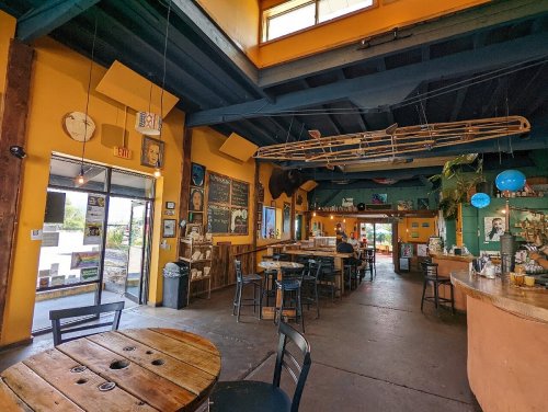 A colorful café interior with wooden tables, chairs, and vibrant walls, featuring artwork and a welcoming atmosphere.