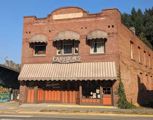 Historic brick building with a striped awning, featuring "Carlson's" and "The Carlson Block" signs.