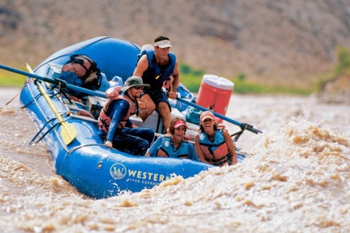 A group of five people in a blue raft navigating through turbulent river waters.