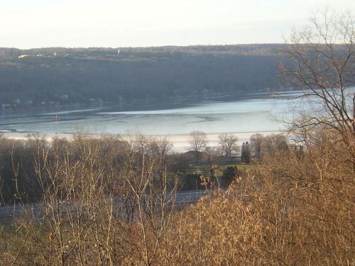 A serene landscape featuring a frozen lake surrounded by trees and hills under a clear sky.