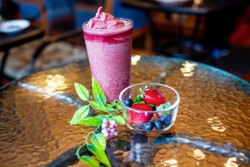 A vibrant berry smoothie in a glass, accompanied by a bowl of fresh strawberries and blueberries on a glass table.