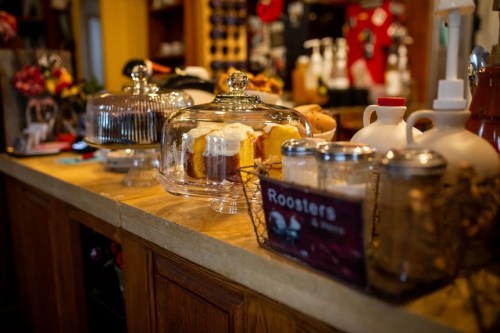 A cozy café display featuring glass cake domes with pastries and a sign for "Roosters" coffee.