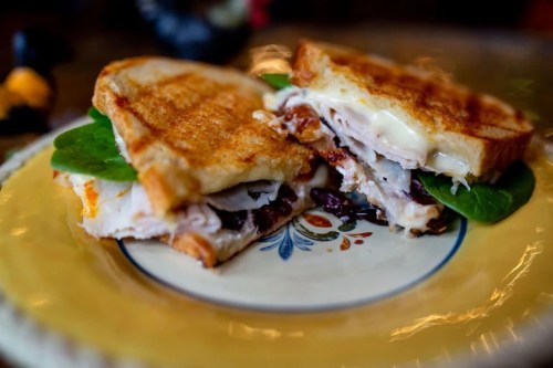 A close-up of a grilled sandwich with turkey, spinach, and melted cheese, served on a decorative plate.
