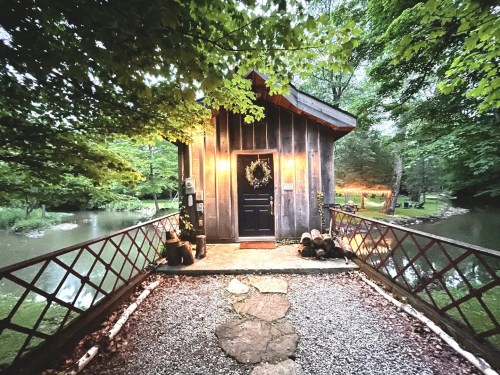 A cozy wooden cabin by a serene pond, surrounded by lush greenery and soft evening light.