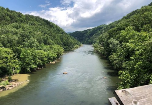 A serene river flows through lush green hills under a partly cloudy sky.