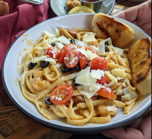 A plate of fettuccine pasta topped with cherry tomatoes, olives, cheese, and served with toasted bread.