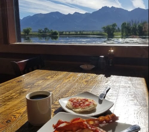 A cozy breakfast setting with bacon, a biscuit topped with jam, coffee, and a stunning mountain view through the window.