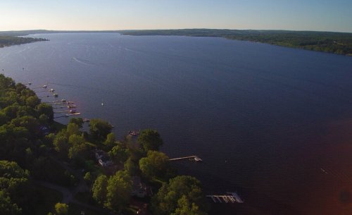 Aerial view of a serene lake surrounded by green trees and small boats on the water under a clear blue sky.