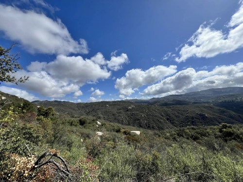 A scenic view of rolling hills under a blue sky with fluffy clouds, surrounded by lush greenery.
