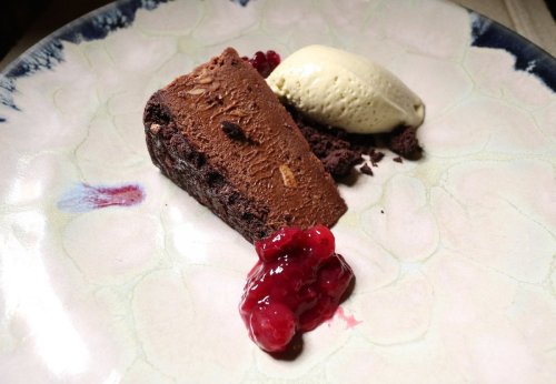 A slice of chocolate dessert with a scoop of vanilla ice cream and a drizzle of berry sauce on a decorative plate.