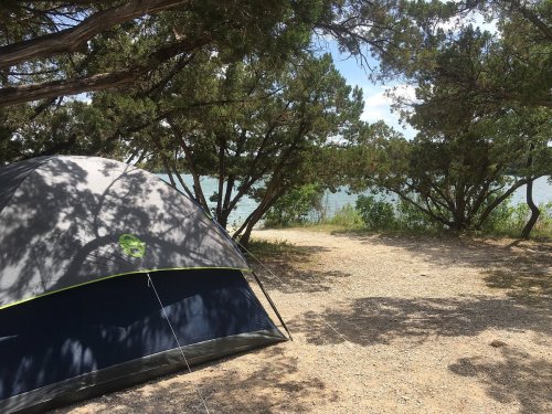 A camping tent set up near a lake, surrounded by trees and a clear blue sky.