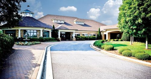 A modern building with a landscaped entrance, surrounded by greenery and a blue sky with clouds.