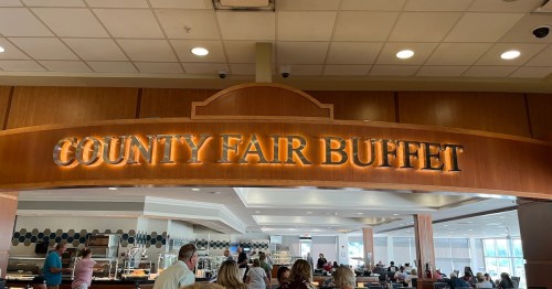 Sign for "County Fair Buffet" above a bustling dining area with people enjoying their meals.