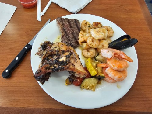A plate of grilled chicken, shrimp, steak, and mixed vegetables on a wooden table.