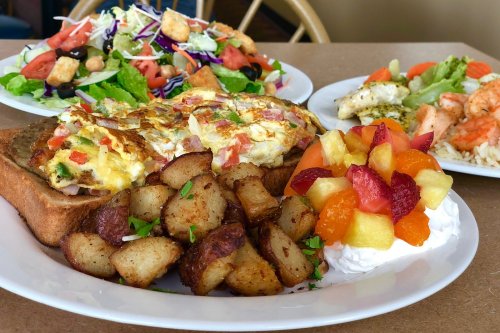 A hearty breakfast plate with an omelet on toast, seasoned potatoes, and a fruit medley, alongside fresh salads.