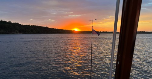 A serene sunset over calm waters, with a flag gently waving on a boat in the foreground.