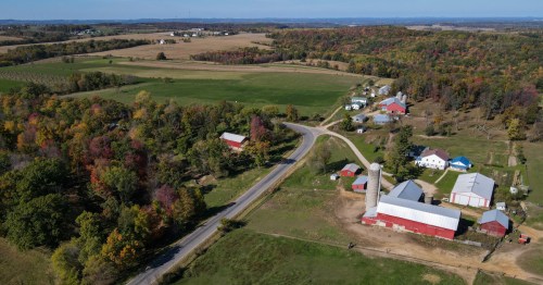 Aerial view of a rural landscape featuring farms, fields, and colorful autumn trees under a clear blue sky.