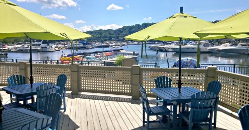 A scenic view of a marina with boats, green umbrellas, and blue chairs on a sunny day.