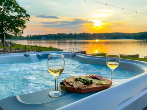 A scenic sunset over a lake, with a hot tub and a platter of snacks and two glasses of white wine in the foreground.