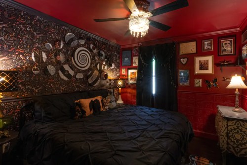 Cozy bedroom with a black bedspread, red walls, eclectic decor, and a chandelier, creating a warm, inviting atmosphere.