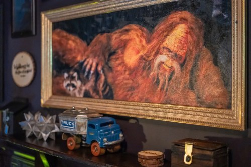 A framed painting of a mythical creature with a raccoon, displayed above vintage toys and decorative items on a shelf.