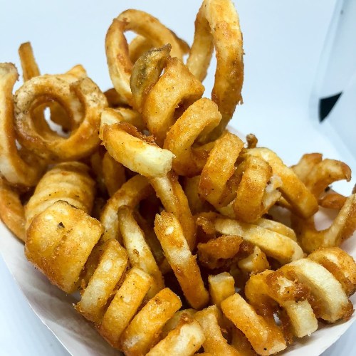A close-up of crispy, golden-brown curly fries piled in a white container.