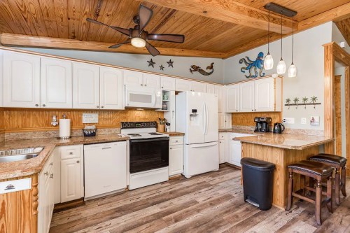 Bright kitchen with white cabinets, granite countertops, and wooden accents, featuring modern appliances and a ceiling fan.