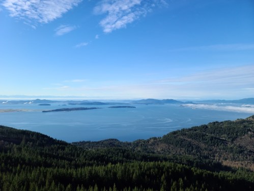 A panoramic view of a blue ocean surrounded by islands and lush green forests under a clear sky.