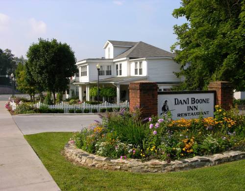 A charming inn with a white exterior, surrounded by colorful flowers and greenery, featuring a sign for Dani Boone Inn Restaurant.