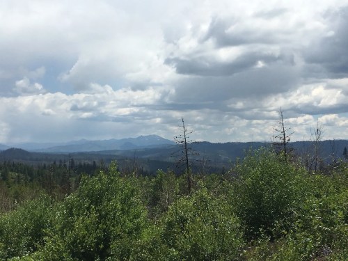 A scenic view of mountains in the distance, surrounded by lush greenery and a cloudy sky.