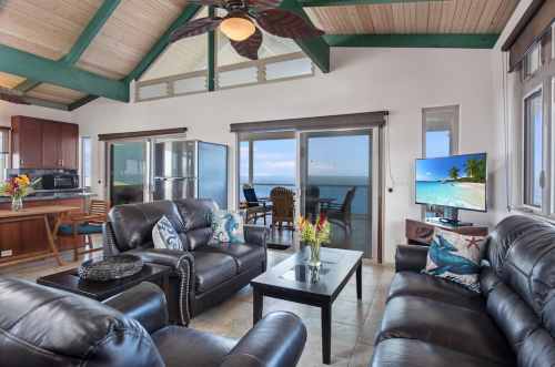 Cozy living room with leather sofas, a coffee table, and a view of the ocean through large windows. Bright and inviting space.
