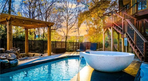 A serene backyard with a pool, wooden pergola, and a treehouse, surrounded by autumn foliage and a sunset sky.