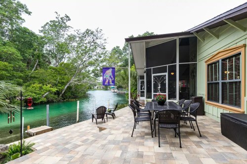 A patio with a dining table overlooks a serene river surrounded by lush greenery.